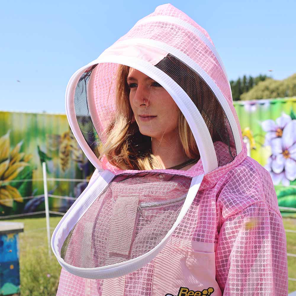 Person wearing a pink beekeeping suit with a hood in an outdoor setting.